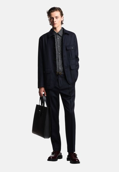 Completo blu navy con camicia a righe bianco e nero con colletto, borsa a tracolla in pelle nera e scarpe bordeaux con finitura liscia.