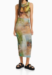 Sopiva, ilman hihoja midi-mekko monivärisessä kiehkurakuviossa, jossa on vihreitä ja ruskeita sävyjä. Yhdistetty mustiin alustalla oleviin sandaaleihin.