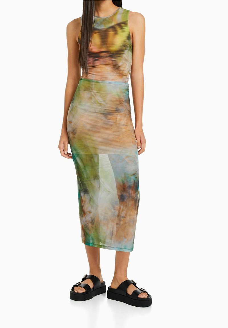 Sopiva, ilman hihoja midi-mekko monivärisessä kiehkurakuviossa, jossa on vihreitä ja ruskeita sävyjä. Yhdistetty mustiin alustalla oleviin sandaaleihin.