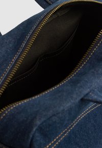 Interior de un bolso de denim con un forro de tela negra. Cuenta con un cierre de cremallera y un pequeño bolsillo interior. Unas costuras doradas acentúan los bordes.