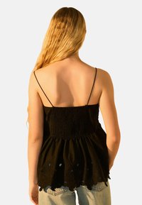 Top noir à bretelles spaghetti avec un corsage smocké et un ourlet évasé, présentant des accents brodés et des détails à bords festonnés.