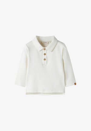 Polo blanc à manches longues avec trois boutons en bois et une petite étiquette marron sur le poignet de la manche gauche.