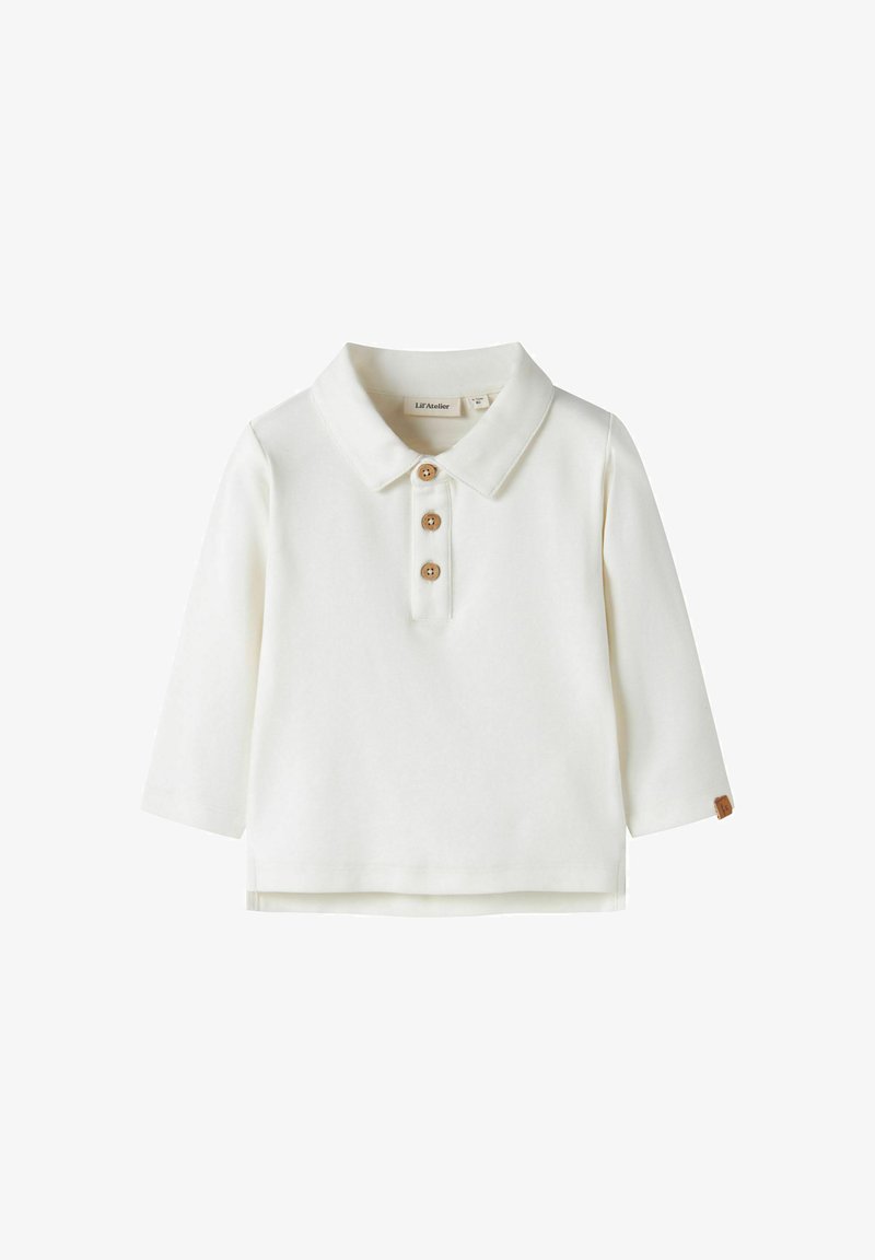 Polo bianca a maniche lunghe con tre bottoni in legno e una piccola etichetta marrone sul polsino della manica sinistra.