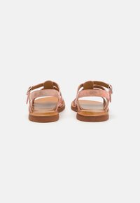 Des sandales en cuir rose présentent un design à lanières avec une fermeture à boucle, une semelle plate et un dos ouvert. Des accents texturés ajoutent un intérêt visuel.