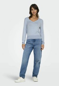 Maglione azzurro chiaro a maniche lunghe con scollo a V, realizzato in materiale morbido, abbinato a jeans larghi e sbiaditi, e sneakers bianche.