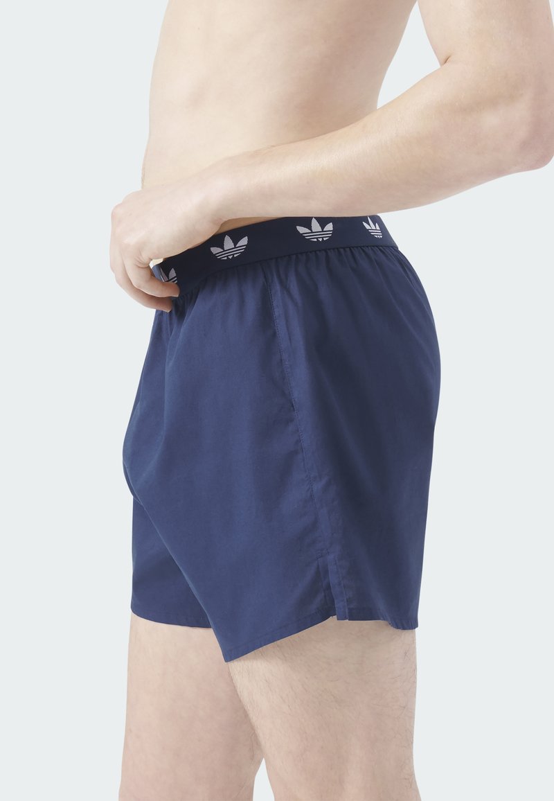 Marineblaue Shorts aus leichtem Stoff mit elastischem Bund und weißem Logomuster. Glatte Oberfläche und schlichtes Design.