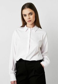 Weißes Hemd mit Knopfverschluss, aus glattem Stoff, mit langen Ärmeln und klassischem Kragen, kombiniert mit schwarzen Hosen. Einfaches und tailliertes Design.