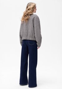 Czarno-biała kurtka w wzór houndstooth z krótkim rękawem i elastycznym pasem, zestawiona z ciemnoniebieskimi spodniami o szerokich nogawkach z wysokim stanem, widoczna od tyłu.