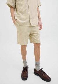 Camisa corta de manga con textura en beige claro combinada con pantalones cortos a juego. Zapatos de cuero marrón y calcetines gris claro completan el look.