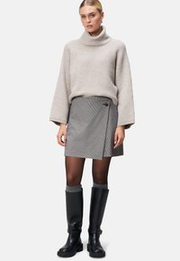 Beige, ribbad polokrage tröja kombinerad med en grå rutmönstrad wrapkjol. Modellen bär svarta knähöga stövlar, vilket ger en lagerlook.
