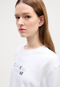 Witte katoenen t-shirt met een ronde halslijn en een voorzijde graphic met de tekst "Calvin Klein Since 1968" in zwarte en zilveren letters.