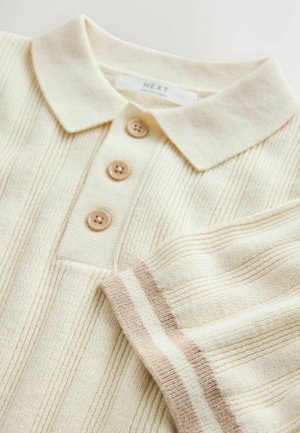 Kortærmet polo-shirt i creme med ribbet tekstur, med tre lysebrune knapper og en stribet kantdetalje i beige nuancer.