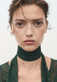 Groene sjaal met een choker-stijl ontwerp, voorzien van ingewikkelde geometrische vormen en texturen, valt elegant om de nek.