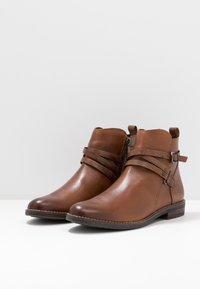 Braune Leder-Stiefeletten mit glatter Oberfläche, ausgestattet mit zwei strukturierten Riemen und einem seitlichen Reißverschluss, auf einem hellen Hintergrund.