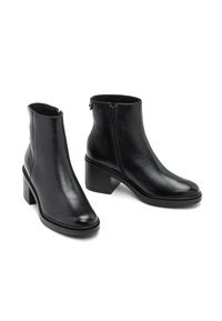 Ett par svarta läderankelboots med blockklackar och sidorekningar på en vit bakgrund.
