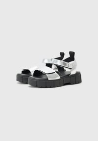 Sandal in argento con due cinture larghe e chiusure in Velcro. Suola spessa in gomma nera con superficie testurizzata. Design open-toe.
