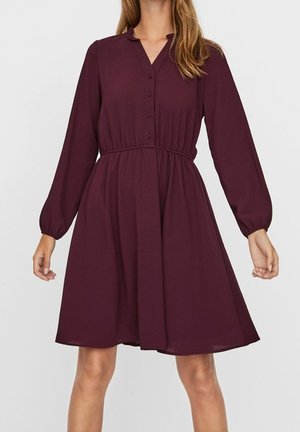 Bordowa sukienka z długim rękawem z przodu na guziki, zebrana w pasie na elastyczną gumkę i z rozkloszowanym dołem. Gładki materiał, luźna sylwetka i klasyczny kołnierzyk.