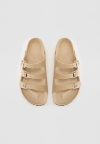 Beige open-toe sandals with three adjustable straps and silver buckles. Soft texture, contoured footbed, and minimalist design.
