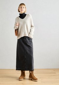 Jersey de punto texturizado beige con escote en V, superpuesto a un cuello de tortuga negro. Una falda midi de mezclilla negra y botas beige con cordones completan el atuendo.