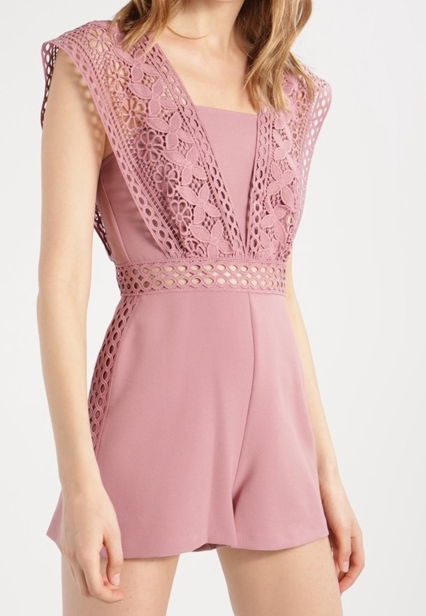 Combinaison courte rose avec des détails en dentelle délicate au niveau de l'encolure et des épaules, dotée d'une taille cintrée et d'un short légèrement évasé.