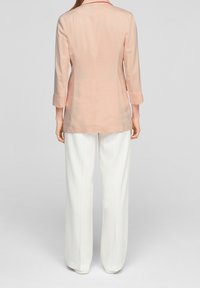Vaaleanpersikanvärinen pusero, jossa istuva leikkaus, pitkät hihat ja kaulus, yhdistetty leveälahkeisiin valkoisiin housuihin. Sileä kangas, minimalistinen muotoilu.