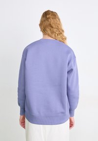 Sudadera de cuello redondo en lavanda clara, con puños y dobladillo de canalé, hecha de una suave tela texturizada. Sin patrones o logos visibles.