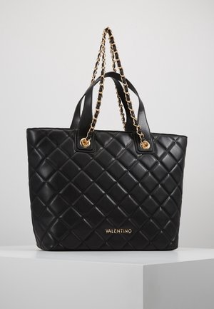 Mustavilla tikattu nahkainen olkalaukku, jossa on kullanväriset ketjuhihnat ja yksityiskohdat. Etupuolella on neliökuvio ja logo. Tasainen pinta.