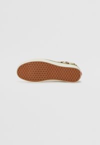 Suela de zapato con un acabado de goma texturizada, que presenta un patrón de panal. El borde circundante es de color crema y tiene una superficie lisa.
