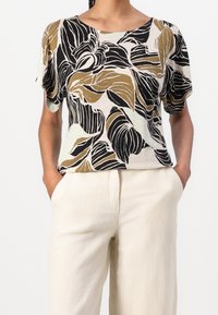 Haut à manches courtes en tissu léger avec un motif floral dans des nuances de noir et de beige. Encolure arrondie et coupe décontractée. Accompagné de pantalons légers.