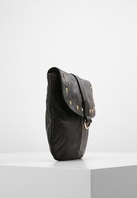 Borsa nera in pelle con patta a piegatura, borchie dorate e dettaglio hardware circolare. La superficie testurizzata aggiunge profondità al design.