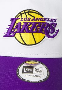 Toacă ajustabilă cu fața albă și marginea violet, având un logo brodat "Los Angeles Lakers" și un grafic de baschet. Inclusă marca New Era.