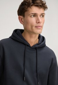 Felpa blu marina realizzata in cotone morbido, con cappuccio regolabile, polsini a coste e un design informale. Minimalista, senza motivi né loghi.