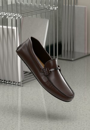 Smeđe kožne loaferice s glatkom površinom, naglašenim šavovima i detaljem od srebrne boje na prednjem dijelu. Lagan dizajn, lagano zaobljen vrh.
