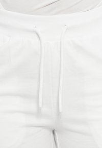 Calças de fato de treino brancas com cintura com cordão, feitas de material macio, com punhos elásticos e textura suave.