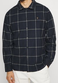 Camicia a quadri blu marina con motivo a griglia bianca, con bottoni sul davanti, colletto e ricamo del logo in modo sottile. Realizzata in tessuto testurizzato.