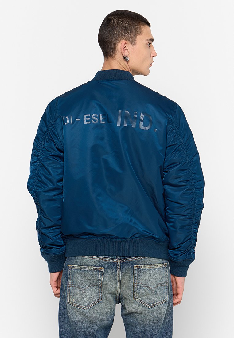 Veste bomber bleu marine avec une finition brillante, poignets et ourlet côtelés, présentant le texte "DI - ESEL IND." en lettres réfléchissantes au dos.