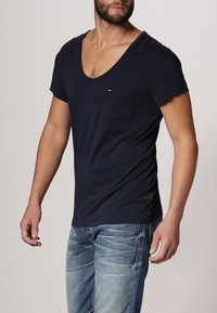 Granatowa koszulka T-shirt z dekoltem w serek i krótkimi rękawami, wykonana z miękkiego materiału, z pojedynczą kieszenią na klatce piersiowej oraz subtelnym logo w rogu.