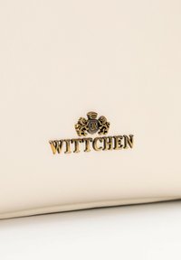 Borsa in pelle sintetica beige con logo in rilievo dorato "WITTCHEN" e dettaglio ornato con crest di leone. Texture liscia, linee pulite.