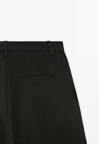 Schwarze Hose aus glattem Stoff mit feiner Textur, Gürtelschlaufen und einer einzelnen Gesäßtasche mit Paspelierung.