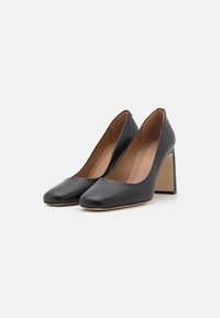 Chaussures à talons en cuir noir avec un bout carré, texture lisse et un talon bloc beige contrastant. Design minimaliste et lignes épurées.
