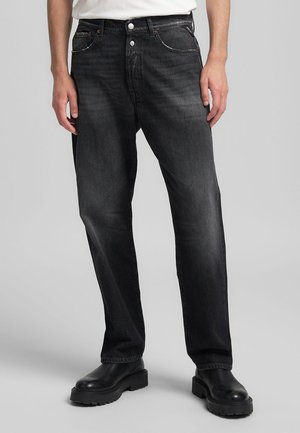 Svarta denimjeans med rak ben-design, kontrasterande sömmar och detaljerade framfickor, i kombination med svarta grova stövlar.