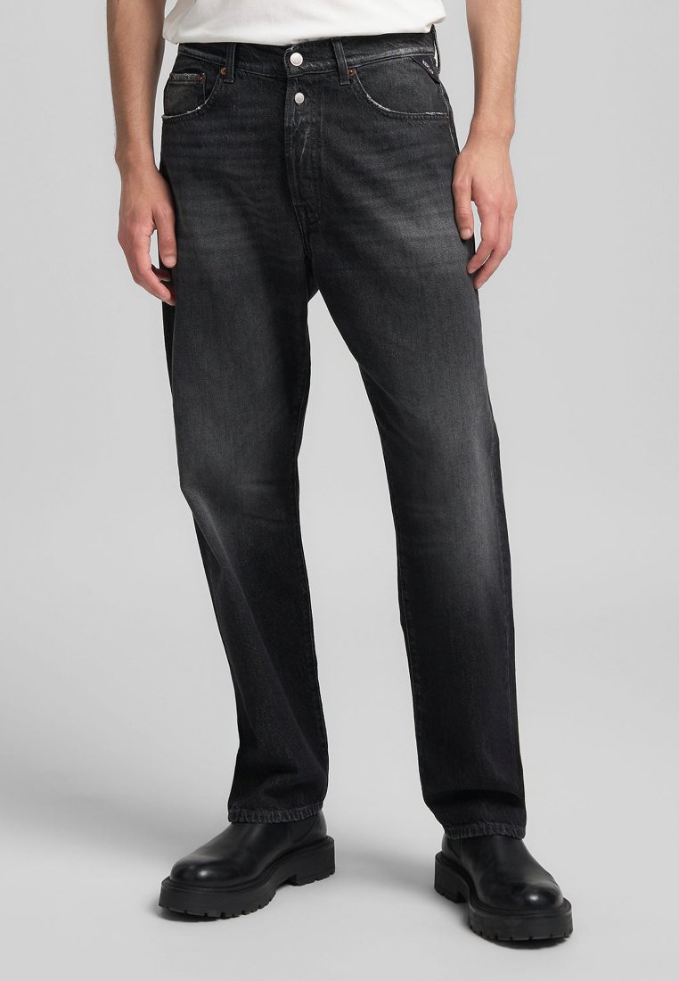 Jean en denim noir avec une coupe droite, des coutures contrastées et des détails de poches avant, associés à des bottes noires chunky.