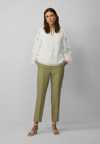 Witte blouse met rimpelende mouwen, keyhole hals, gecombineerd met olijfgroene op maat gemaakte broek en witte strappy hakken. Eenvoudige, elegante look.