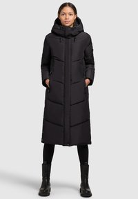 Długi czarny puchowy płaszcz z kapturem, z pionowymi przeszyciami, kieszeniami bocznymi i zapięciem na napy u dołu. Wykonany z pikowanego, ocieplanego materiału.