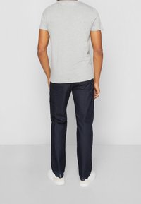 Camiseta gris de manga corta combinada con pantalones de mezclilla oscuros, con bolsillos traseros y un ajuste relajado. Zapatillas blancas informales completan el look.