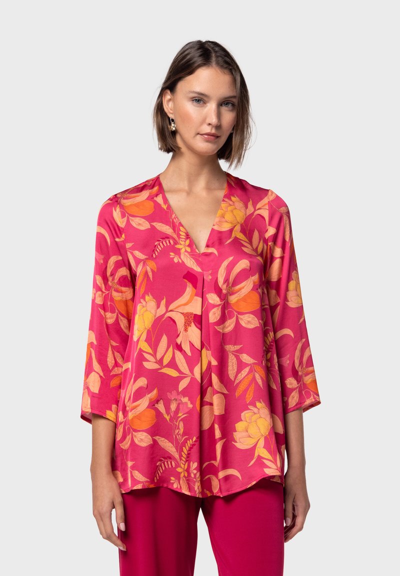 Blusa floral en rosa con estampados en naranja y amarillo, diseño de escote en V, mangas tres cuartos y un corte holgado, combinada con pantalones lisos rosas.