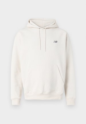 Sahnefarbener Kapuzenpullover mit Fronttasche, Kordelzug an der Kapuze und kleinem, dunklem New Balance Logo auf der Brust.