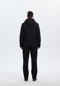 Veste imperméable noire avec capuche, présentant une texture lisse et un design minimaliste. Associée à un pantalon noir assorti pour un look coordonné.