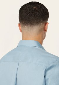 Lichtblauwe shirt met een geribbelde textuur, een klassieke kraag en een klein geborduurd logo op de achterkant. Netjes afgewerkt en eenvoudig ontwerp.