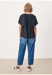 Haut bleu marine à manches courtes avec encolure froncée, associé à un jean bleu clair à coupe décontractée et des baskets blanches avec des accents bordeaux.